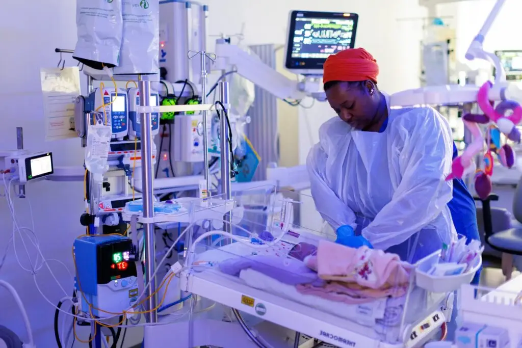 A nurse in a red headband tending to a baby in an incubator