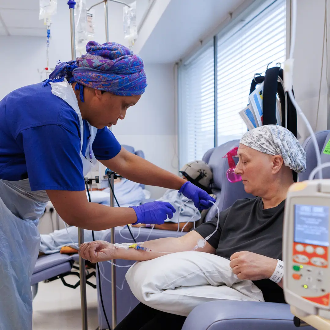 Woman with headscarf receiving chemotherapy as a nurse attends to her