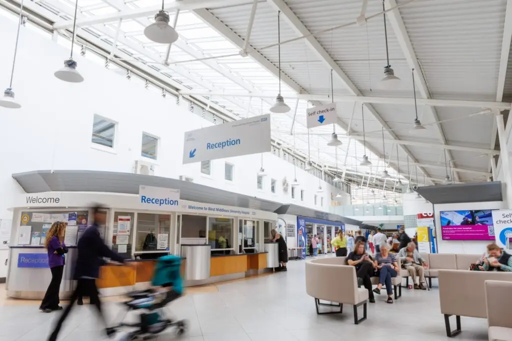Lobby area of West Middlesex University hospital with people walking past and sitting near a reception area
