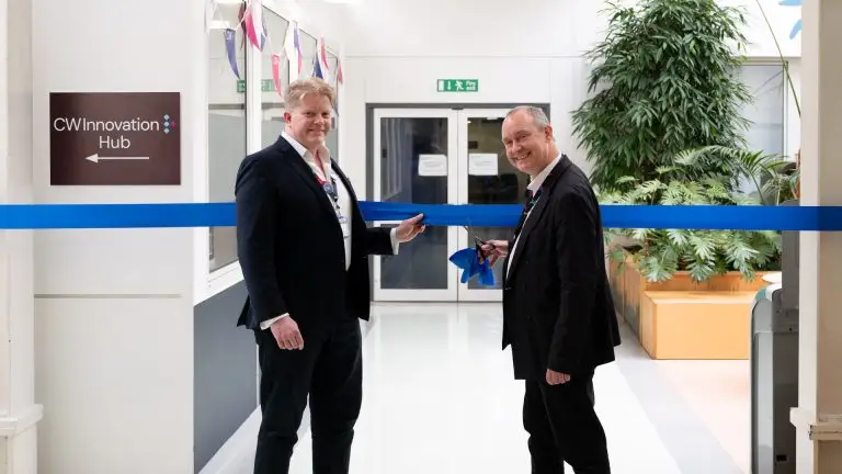 Two smiling men in suits, about to cut the ribbon to open the new CW Innovation Hub at Chelsea and Westminster Hospital