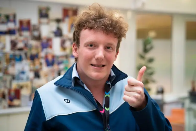 Young man wearing a hospital porter top smiling and doing a 'thumbs' up sign