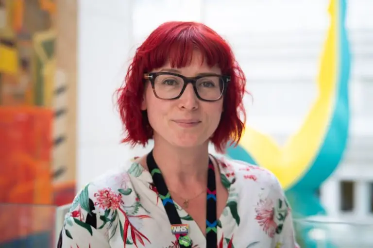 Female with cropped red hair and glasses smiling at the camera. She is an art psychotherapist at Chelsea and Westminster Hospital. Art psychotherapy