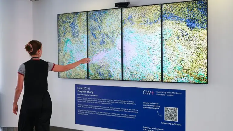 Woman with an outstretched arm walking past an interactive digital artwork - four large screens displaying dynamic swirling colourful ripples