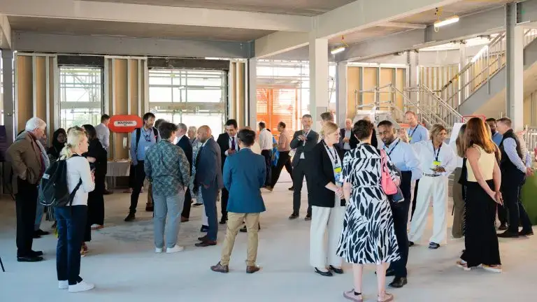 People mingling and networking at an event. They are standing in a large unfinished space (the structure of the new £80m centre at West Mid)