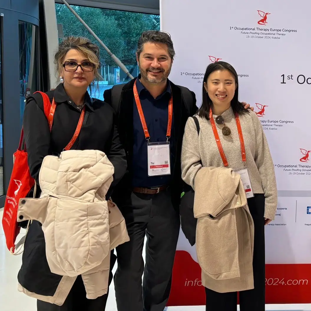 Two women and a man wearing lanyards next to a conference banner
