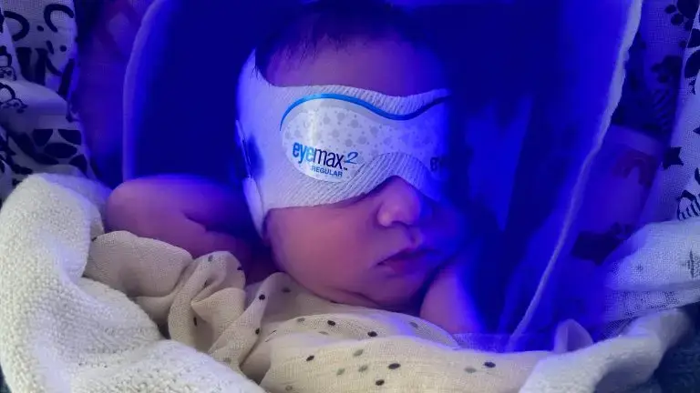 Very small baby wearing a mask covering his eyes, with a blue-ish light surrounding him
