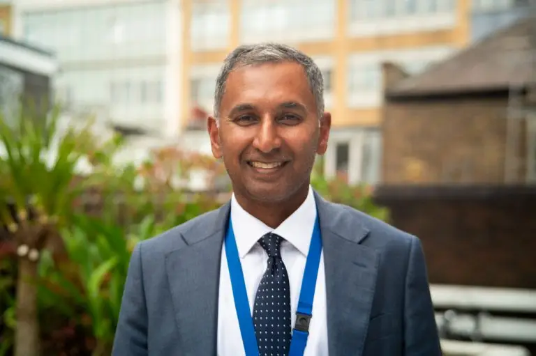 Headshot of an Asian man smiling at the camera. He has short grey hair and is wearing a grey suit, white shirt, black tie and has a lanyard around his neck. He is a cardiologist who talks about why the new centre at West Mid Hospital is a game changer, and how you can 'buy a brick' to support it