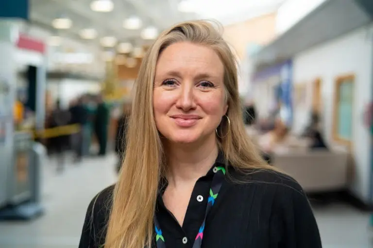 CW+ Writer in Residence, Rebecca Goss. A white woman with long blond hair smiling at the camera. She is wearing a black shirt.