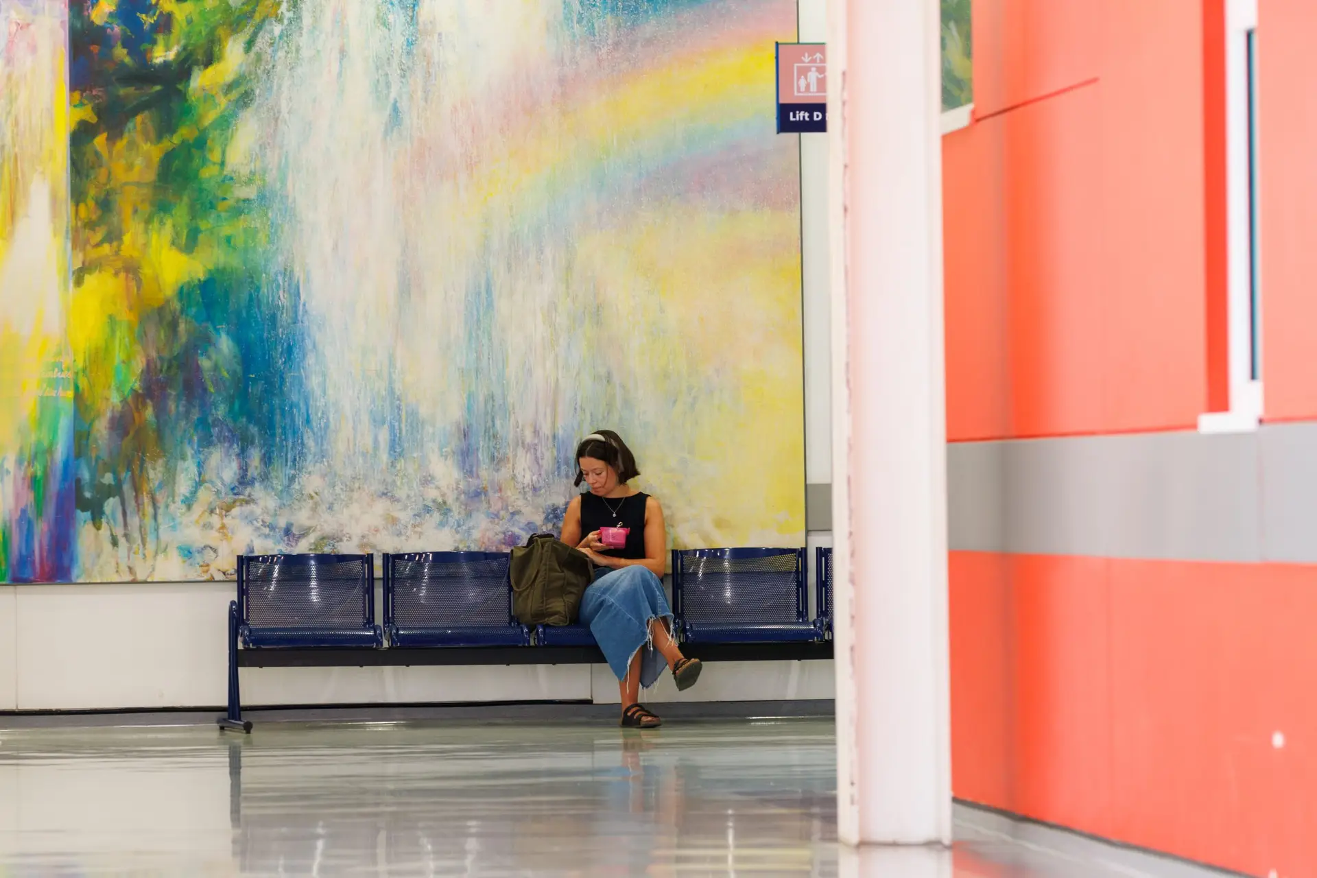 A woman in a black top is sitting in front of a large-scale artwork on a hospital wall